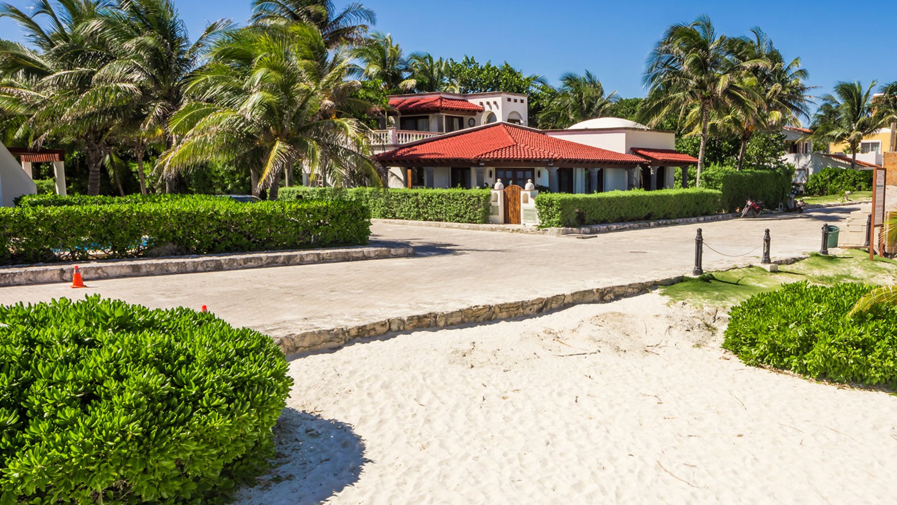 A 1990s villa in Playacar Fase 1 with white masonry and a terracotta tile roof, seen from the beach road