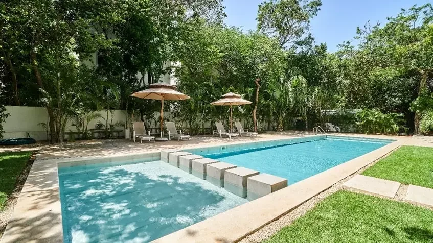 Alberca y terraza de asoleadero de un condominio en Selvamar, con sombra de los árboles y un chapoteadero al frente