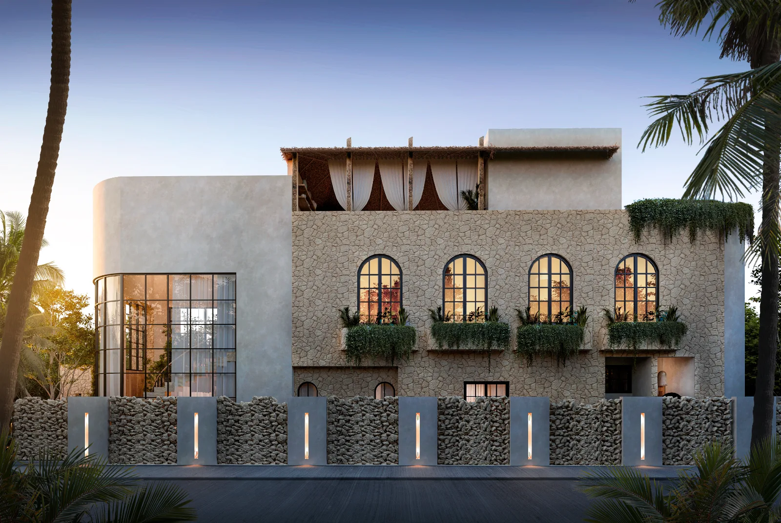 Fachada de una villa en la Riviera Maya al atardecer, muro de piedra caliza y ventanas de arco iluminadas