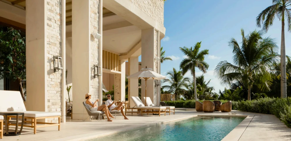 Owners on the shaded pool terrace at Costa Residences, Corasol, palms and stone colonnade behind