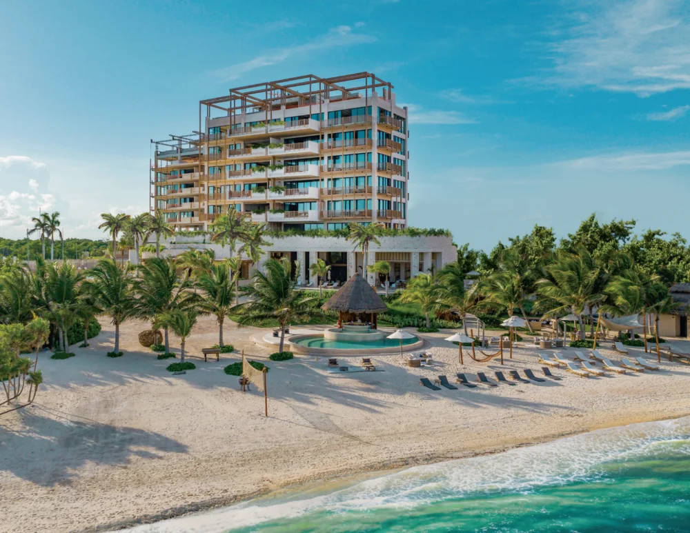 Costa Residences at Corasol seen from the beach, stone and timber tower behind the palapa pool and sand