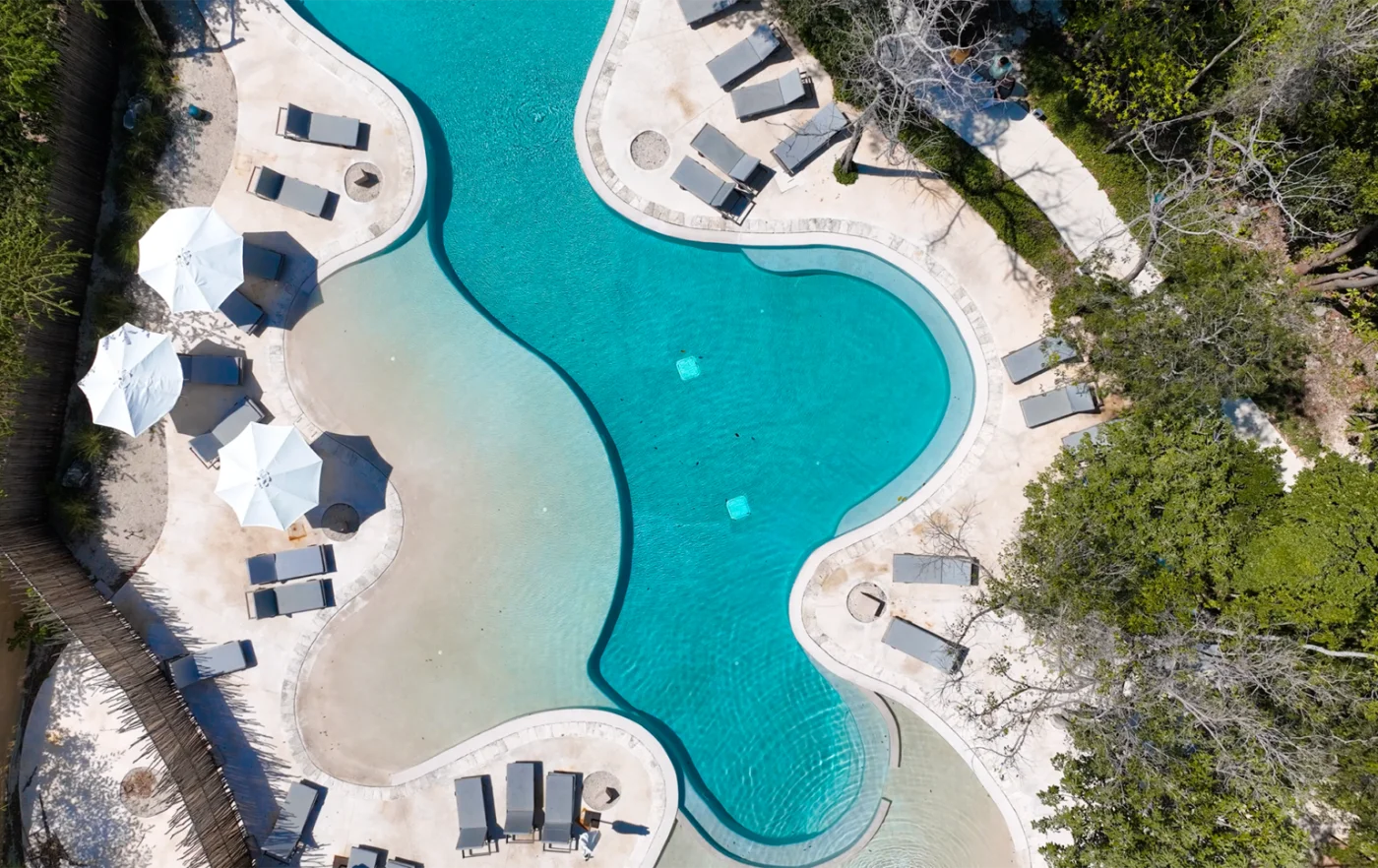 Overhead view of the sand entry family pool at The Village, Corasol, loungers and umbrellas along its edge