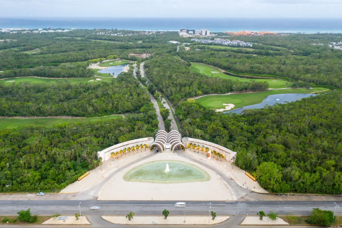 Vue aérienne de l'entrée principale de Corasol sur la route fédérale 307, le bâtiment d'accueil à arcades et la fontaine, avec le golf et les Caraïbes derrière