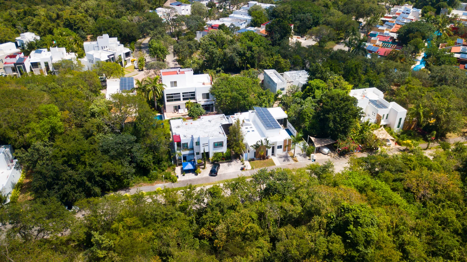 A street of houses inside El Cielo Residencial seen from the air, jungle between the blocks and the city beyond