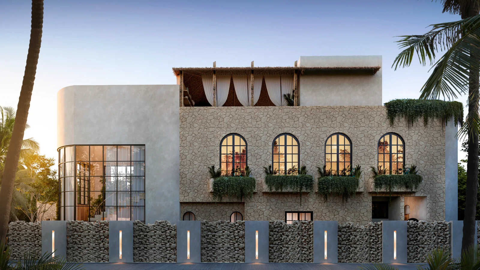 Facade of a new villa in the Riviera Maya at dusk, chukum stucco, arched steel windows and a stone perimeter wall