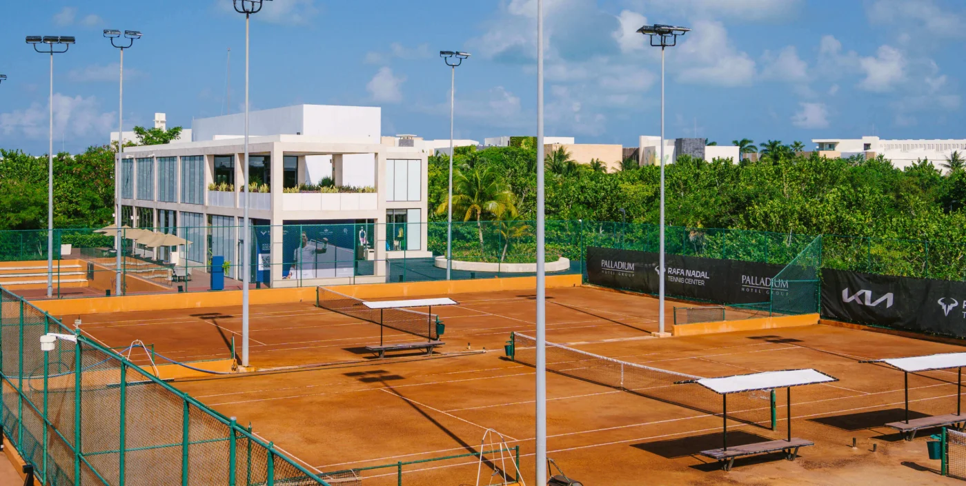 Les courts en terre battue et le club house de deux niveaux du Rafa Nadal Tennis Center au Grand Palladium Costa Mujeres, mâts d'éclairage et bâches Palladium le long de la clôture