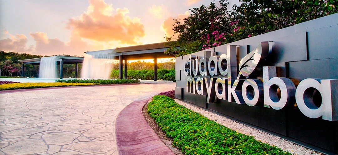 Ciudad Mayakoba entrance sign at sunset with the water wall and access canopy behind it