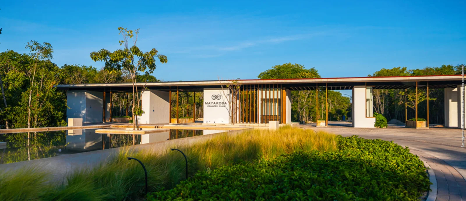 Entrance of the Mayakoba Country Club clubhouse, white walls with timber louvres reflected in a shallow water feature