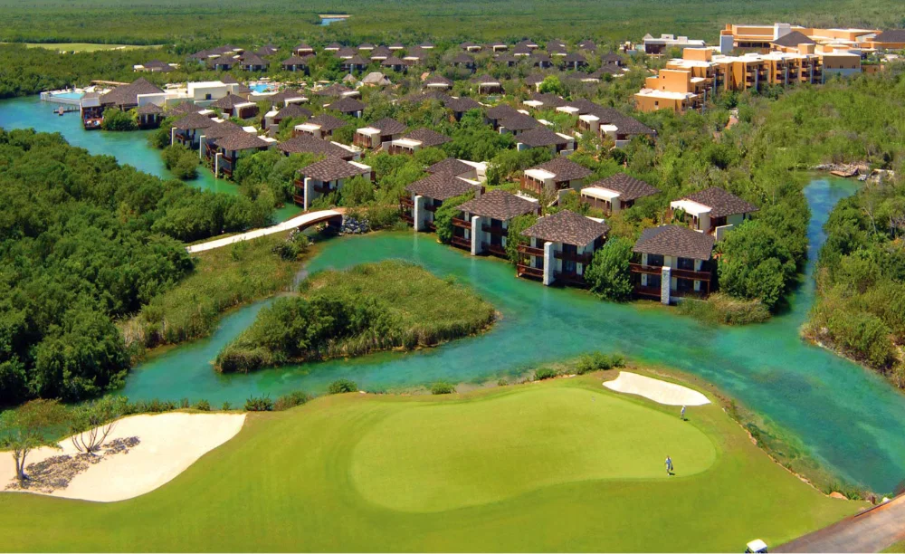 Alberca infinita y terraza de madera frente al Caribe en Mayakoba, con palmeras a contraluz del amanecer