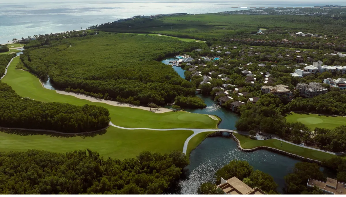 Vue aérienne d'El Camaleón à Mayakoba : un green entre un canal de mangrove et les villas du resort, les Caraïbes au fond