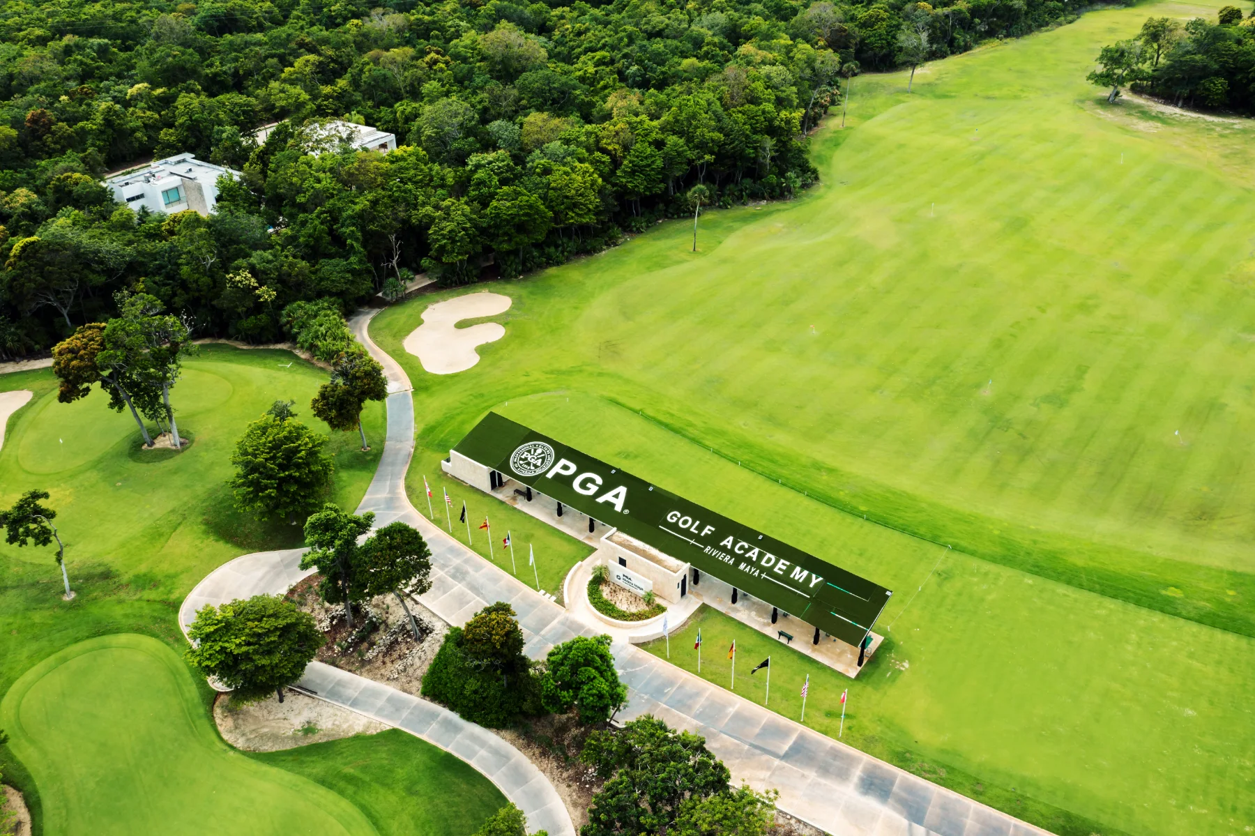 Aerial of greens and turquoise lakes at PGA Riviera Maya with the entrance arch, the Bahía Príncipe hotels and the Caribbean behind