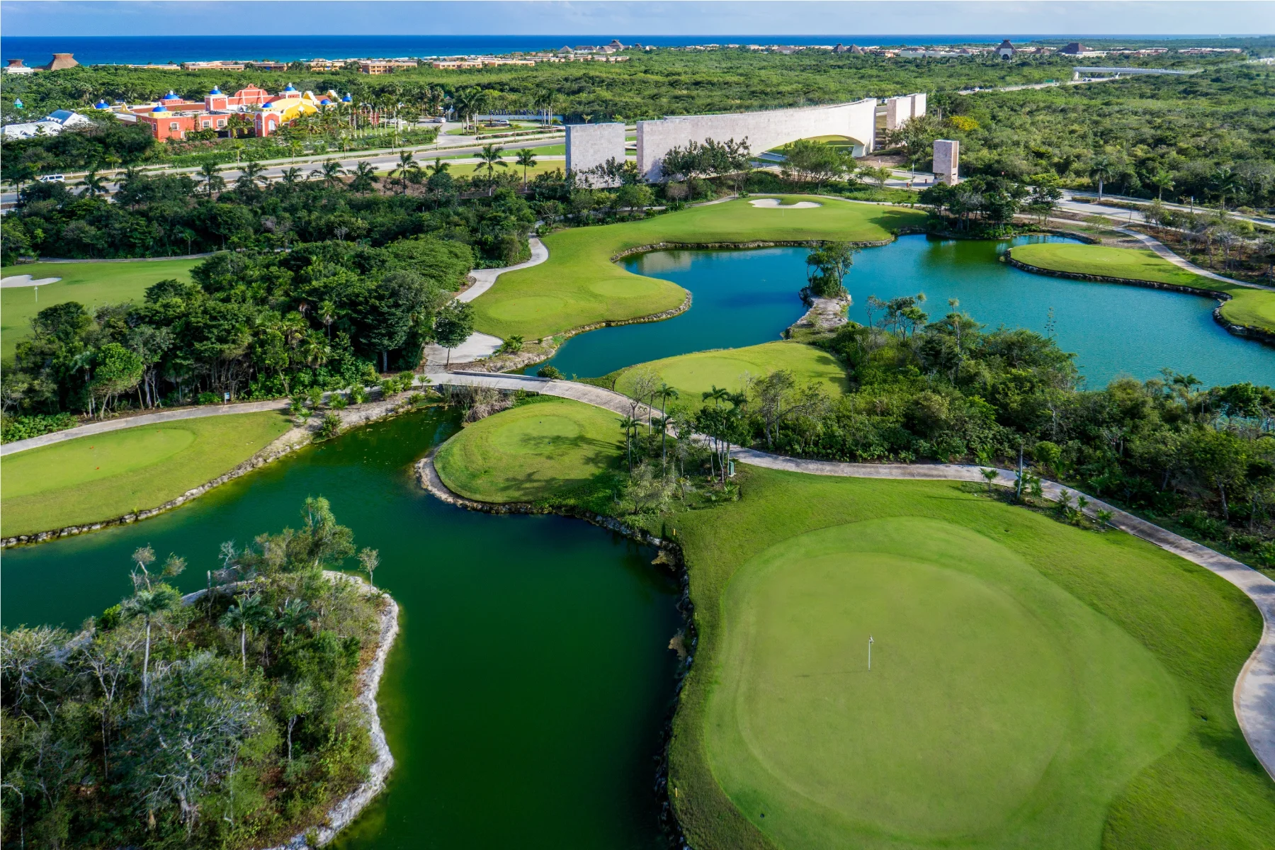 Aerial of the PGA Riviera Maya course, the practice range and the clubhouse parking with the Caribbean on the horizon