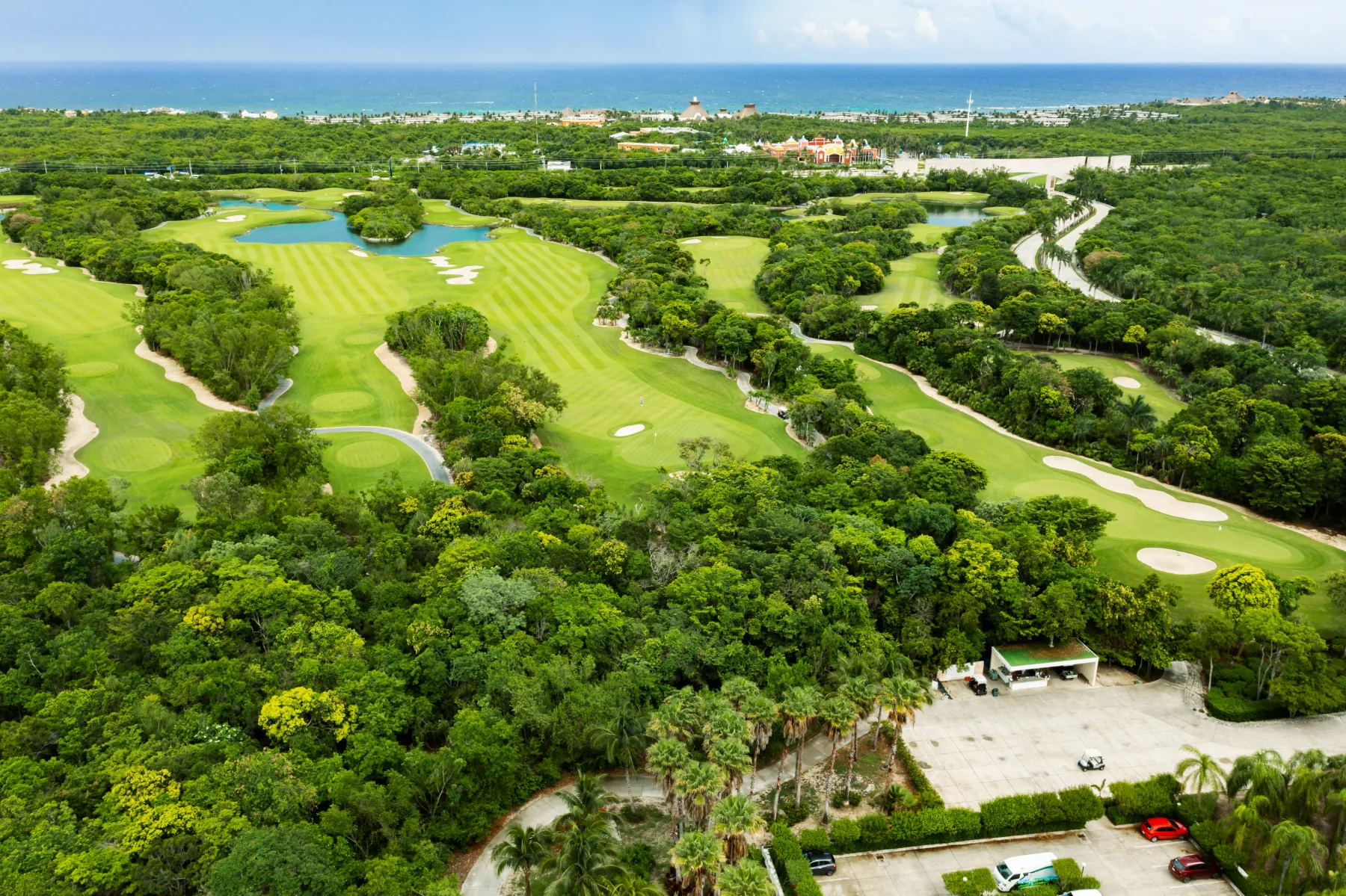 Vista aérea de un fairway rayado en el PGA Riviera Maya junto a un lago turquesa de borde de piedra caliza y un green isla
