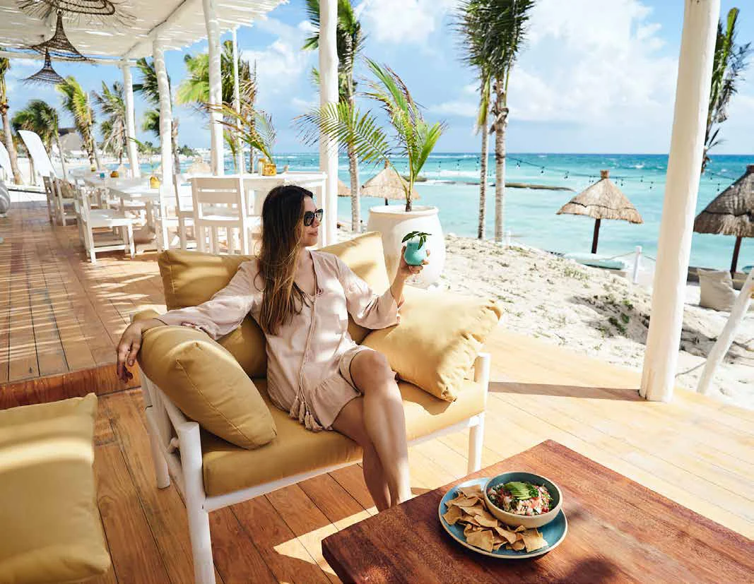 Terrasse en bois du Kay Beach Club avec mobilier de lounge, palmiers et les Caraïbes au fond