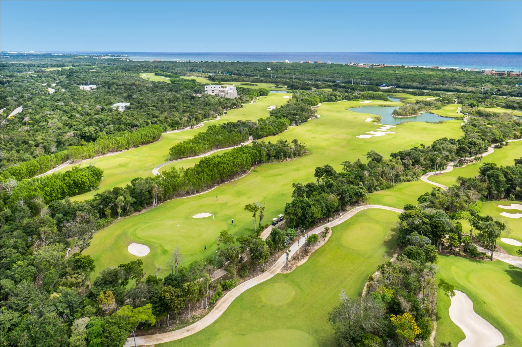 Vue aérienne le long des fairways du PGA Riviera Maya vers les Caraïbes, des golfeurs sur le green et la jungle entre les trous